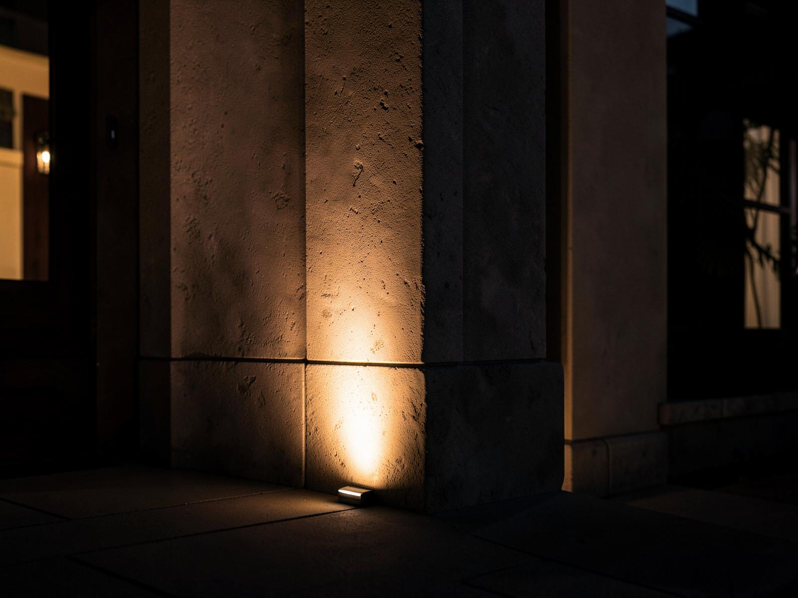 Warm residential uplighting emphasizing a stone column and entry